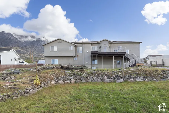 Two-story home with horizontal siding, elevated rear deck with staircase, and terraced stone retaining wall, set against a mountainous backdrop