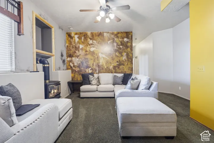 Freestanding wood-burning stove with metal chimney, decorative accent wall, ceiling fan with integrated lighting, and wall-mounted shelving niche