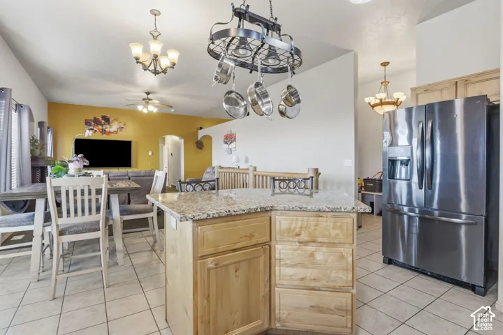 Kitchen featuring a center island with light wood cabinetry, stone-finish countertops, stainless steel French-door refrigerator, and a wrought-iron hanging pot rack