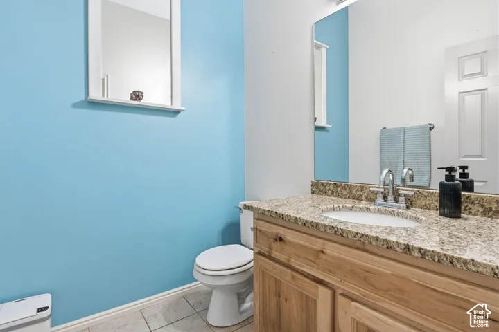 Vanity featuring a stone-composite countertop, undermount sink, dual-handle faucet, and natural wood cabinetry, complemented by a large wall-mounted mirror and tile flooring