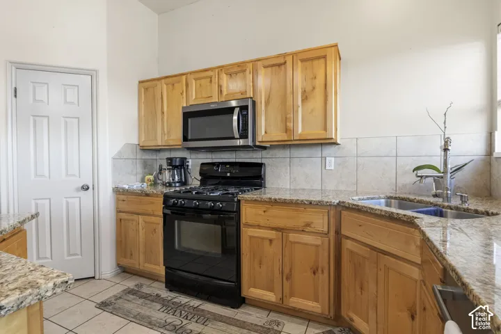 Kitchen featuring natural wood cabinetry, stone-surface countertops, tile backsplash, stainless steel microwave, and dual-basin stainless steel sink