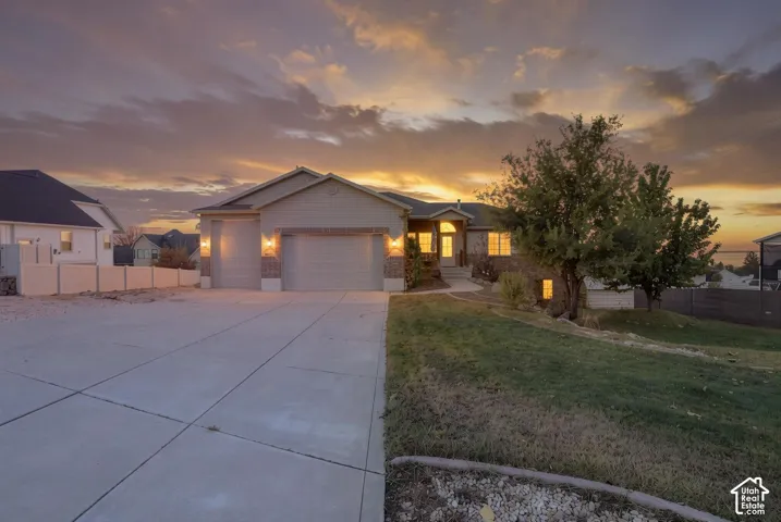 Single-level residence with a multi-car garage, brick and siding exterior, concrete driveway, and expansive lawn under a sunset sky