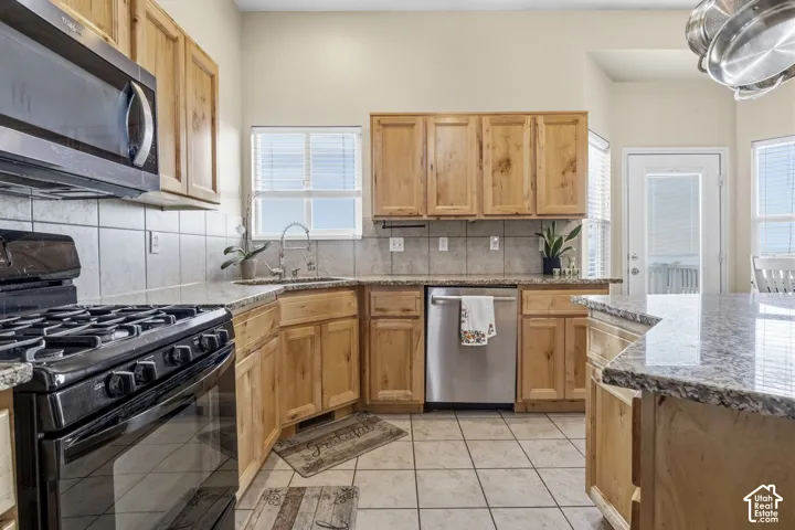 Kitchen featuring knotty wood cabinetry, stone-patterned countertops, a stainless steel appliance package, tile flooring, and a subway tile backsplash