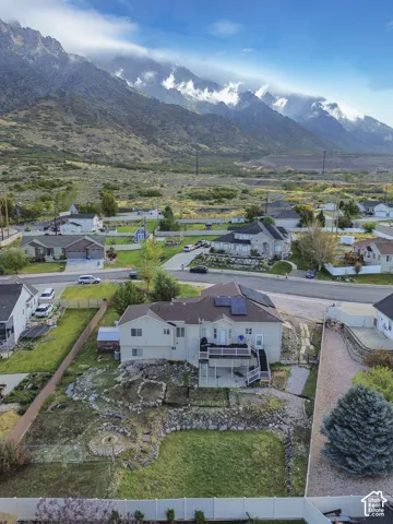 Aerial perspective featuring an elevated deck, solar panel array, terraced stone retaining walls, and a private rear lawn, all set against a prominent mountain backdrop