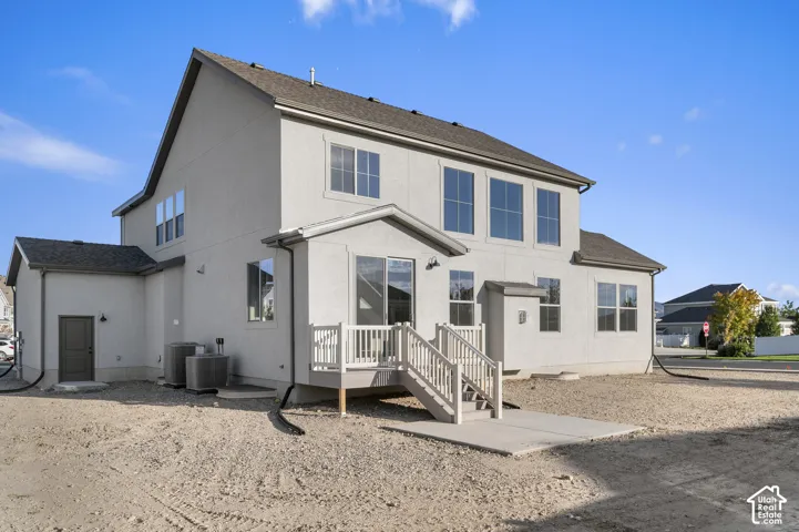 Two-story stucco exterior featuring a composite shingle roof, raised wood deck with staircase, concrete patio, and grid-pattern windows