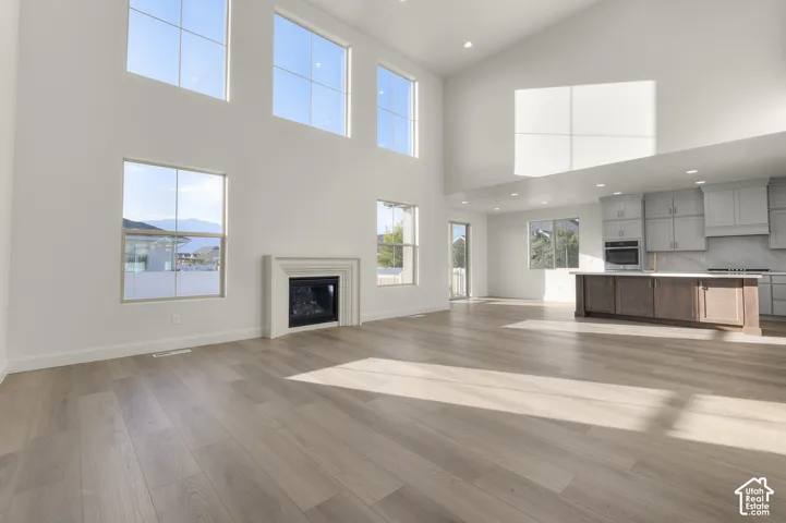 Double-height ceiling with multi-level windows, wood-finish flooring, fireplace with a tiered mantel, recessed lighting, and a kitchen island with built-in cabinetry