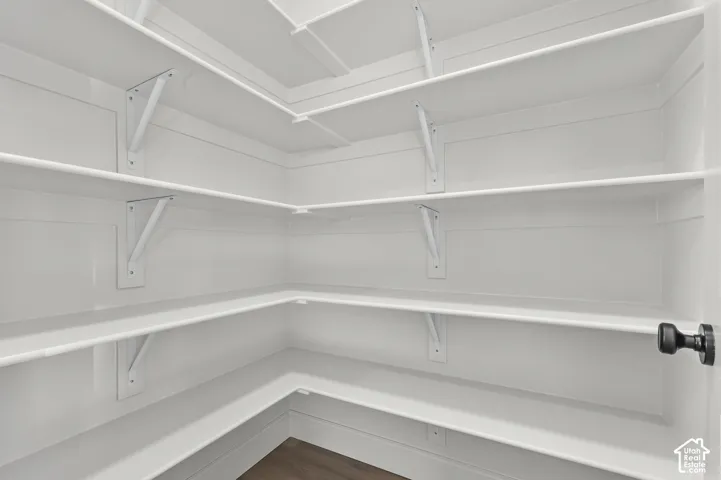 Walk-in pantry featuring white wrap-around shelving, structural wall-mounted brackets, and wood-finish flooring
