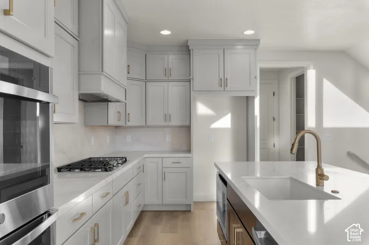 Kitchen featuring shaker-style cabinetry, quartz countertops, a central island with an undermount sink, a gas cooktop, and built-in stainless steel double ovens