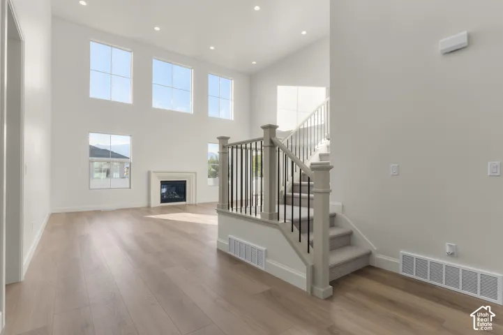 Two-story ceiling height, wood-finish flooring, recessed lighting, fireplace with stone-finish surround, and a staircase featuring a painted wood railing with metal balusters