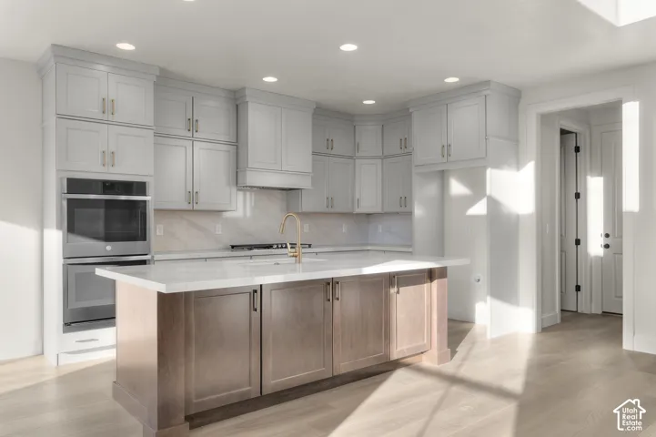 Kitchen featuring light-toned cabinetry, a contrasting wood-finish island, solid-surface countertops, stone-finish backsplash, and built-in double wall ovens