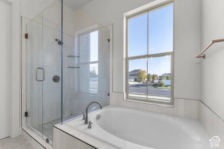 Walk-in shower with a glass enclosure, soaking tub with a deck mount faucet, large window, and metallic fixtures