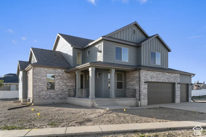 Two-story residence featuring a blend of horizontal siding and board-and-batten siding, stone-veneer masonry, a covered front porch with metal railing, and an attached three-car garage