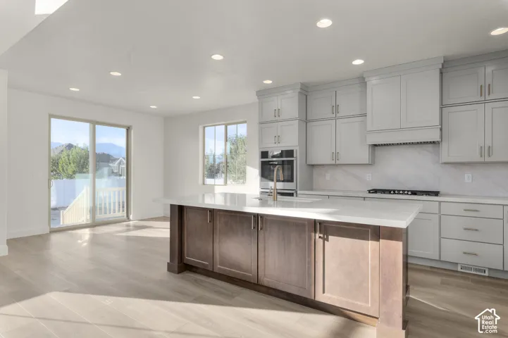 Kitchen featuring a central island with wood-finish cabinetry, quartz countertops, light-gray shaker-style cabinetry, recessed lighting, and wood-finish flooring
