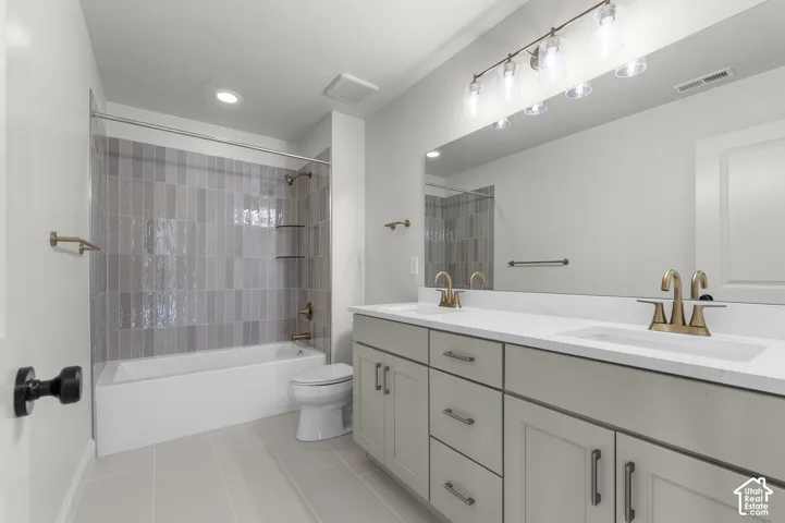 Double vanity featuring a light-toned cabinetry, solid surface countertop, metallic hardware, and oversized wall-to-wall mirror with multi-bulb vanity lighting