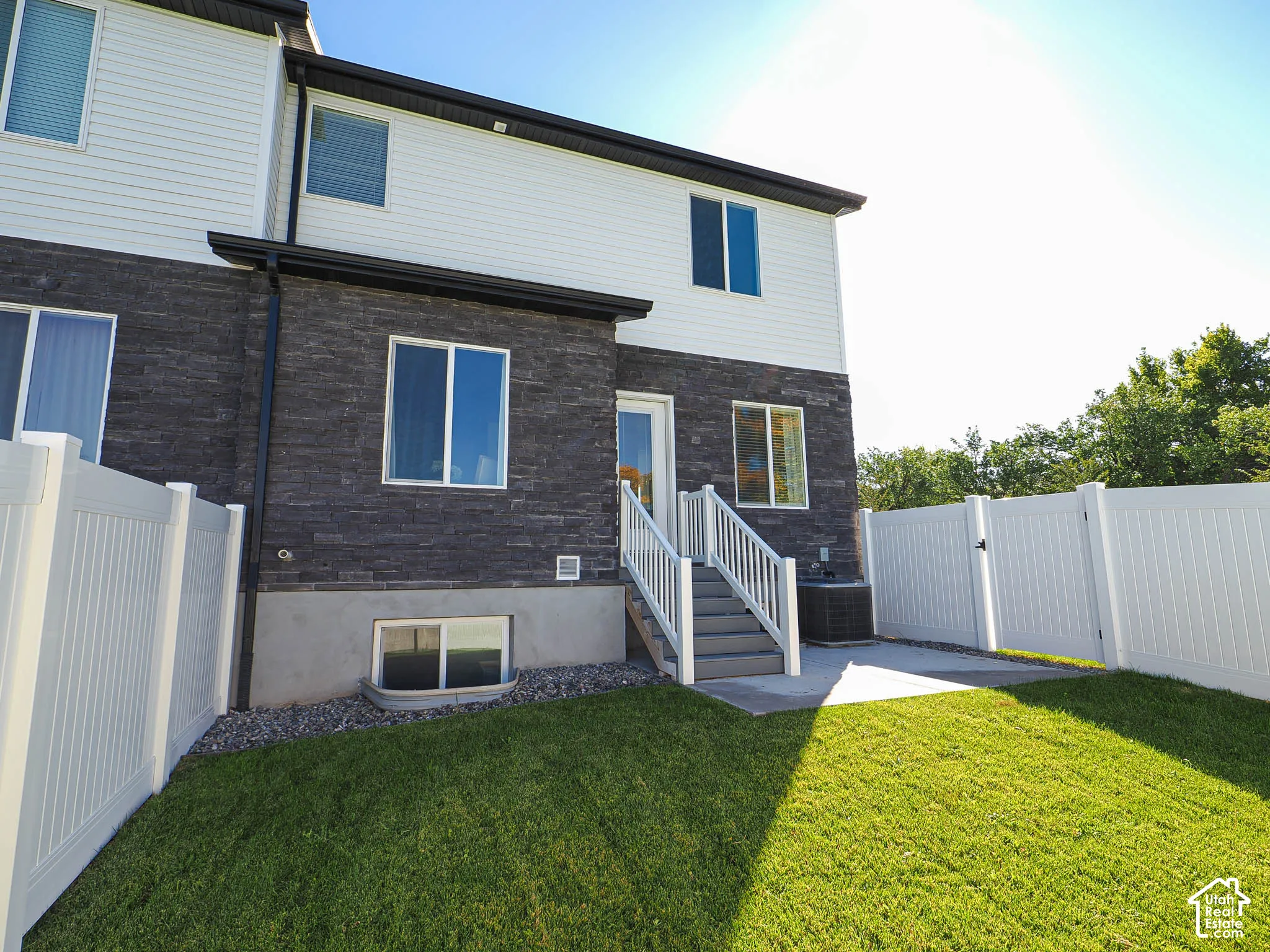 Exterior featuring a combination of horizontal siding and stone veneer, private white vinyl fencing, a concrete patio, and a set of exterior stairs with a white railing