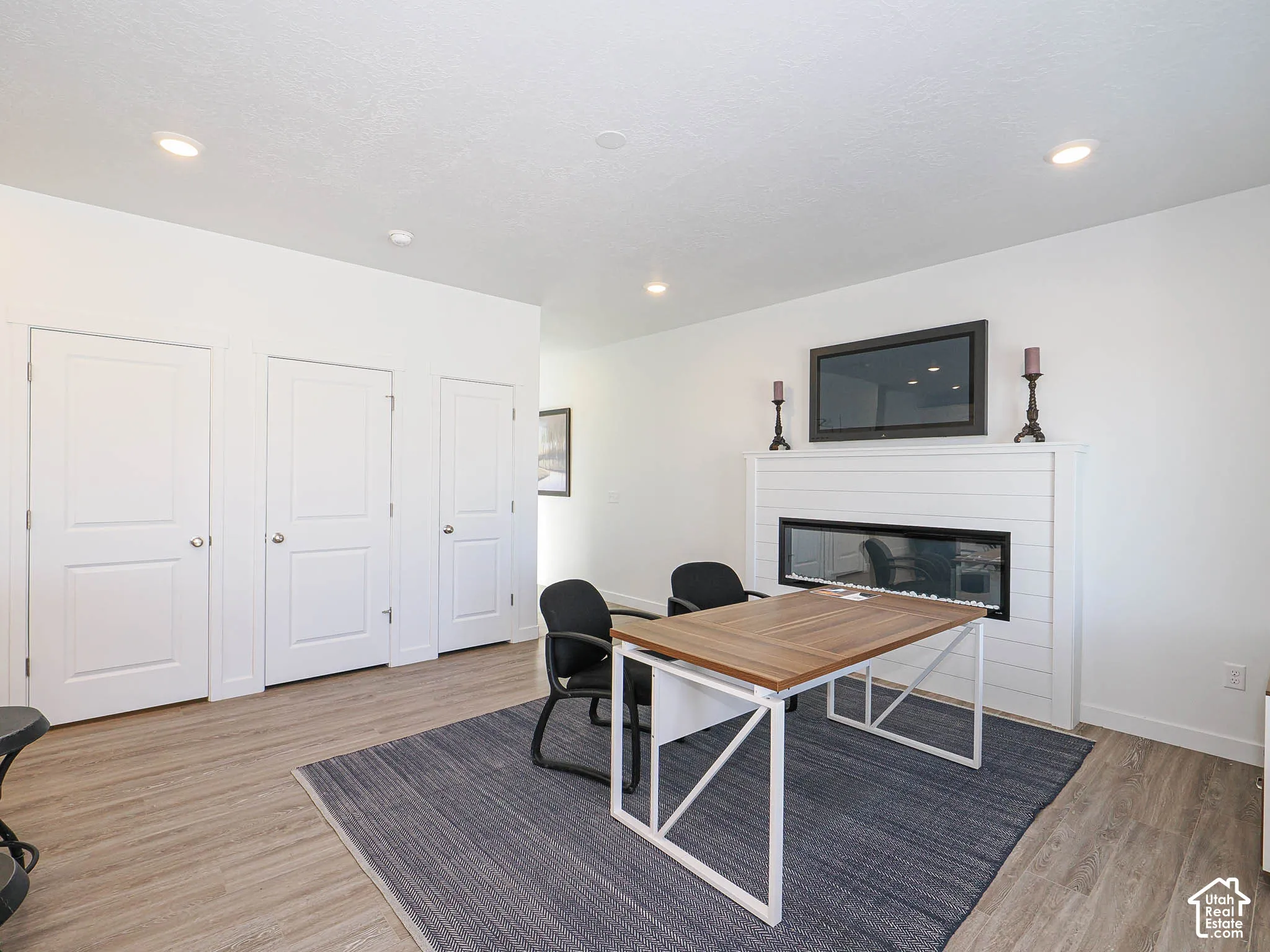 Room interior featuring wood-finish flooring, recessed lighting, white panel doors, and a linear fireplace with white shiplap-style surround