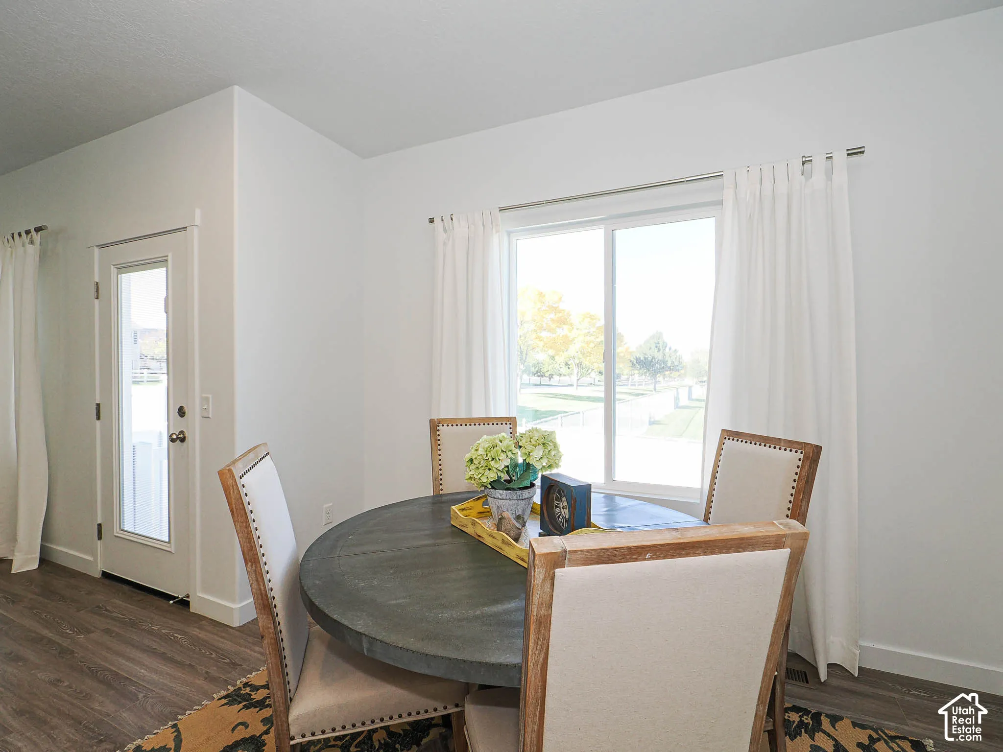 Neutral-toned room featuring wood-finish flooring, a glass-paneled entry door, and a sliding window with metallic curtain hardware