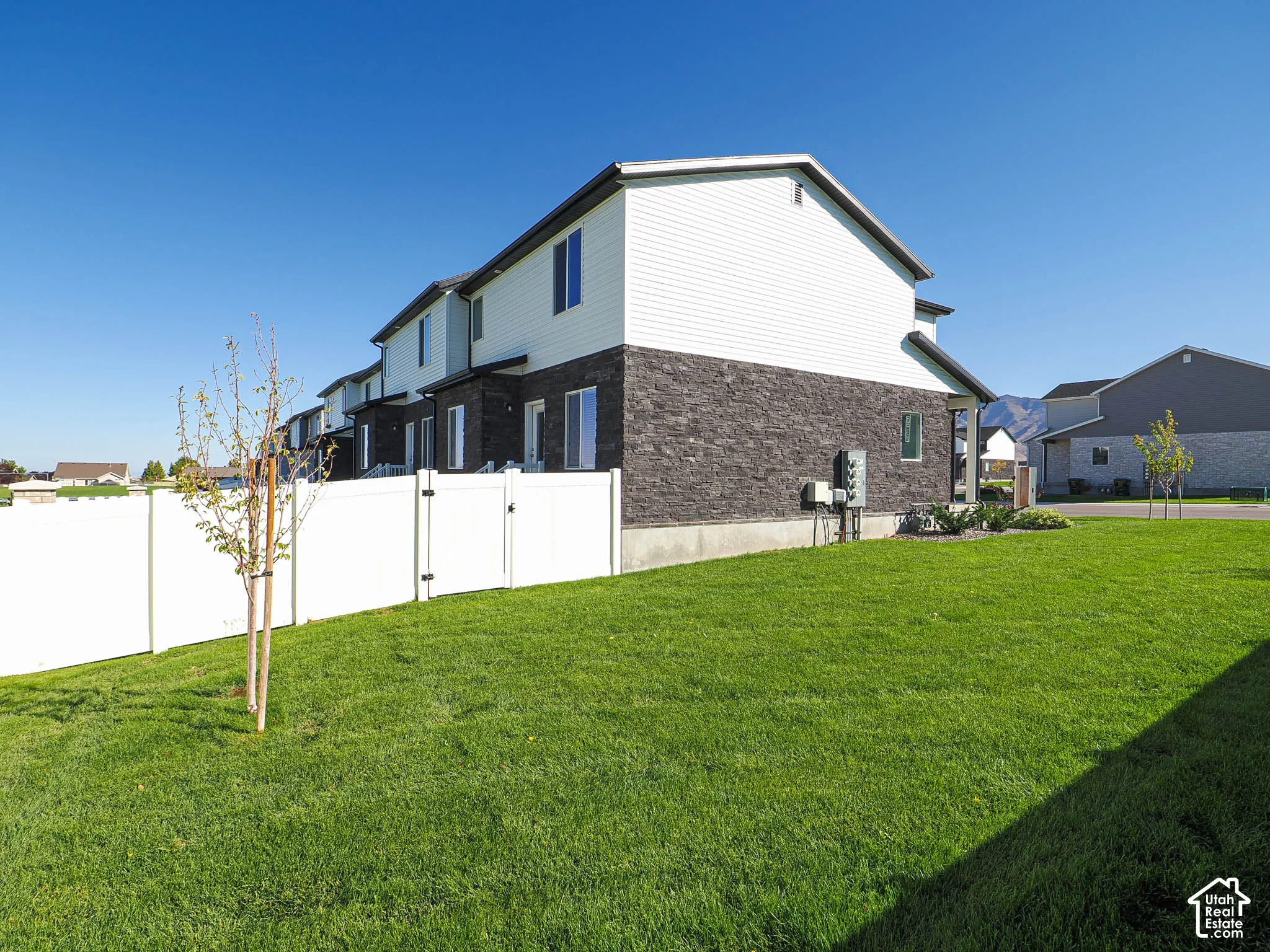 Multi-level exterior featuring white vinyl siding, dark stone veneer, a white vinyl privacy fence, and a manicured lawn