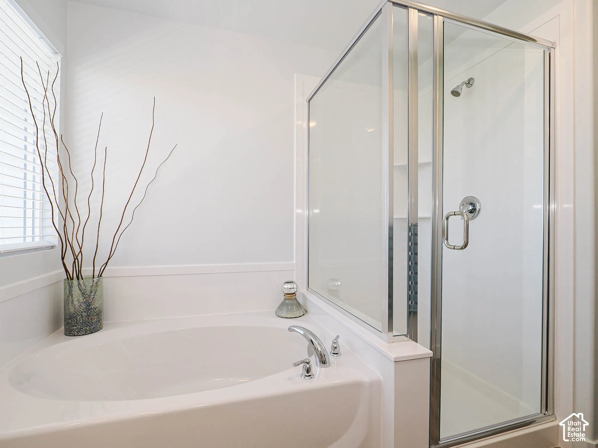 Oval soaking tub with chrome fixtures, accompanied by a separate glass-enclosed shower stall
