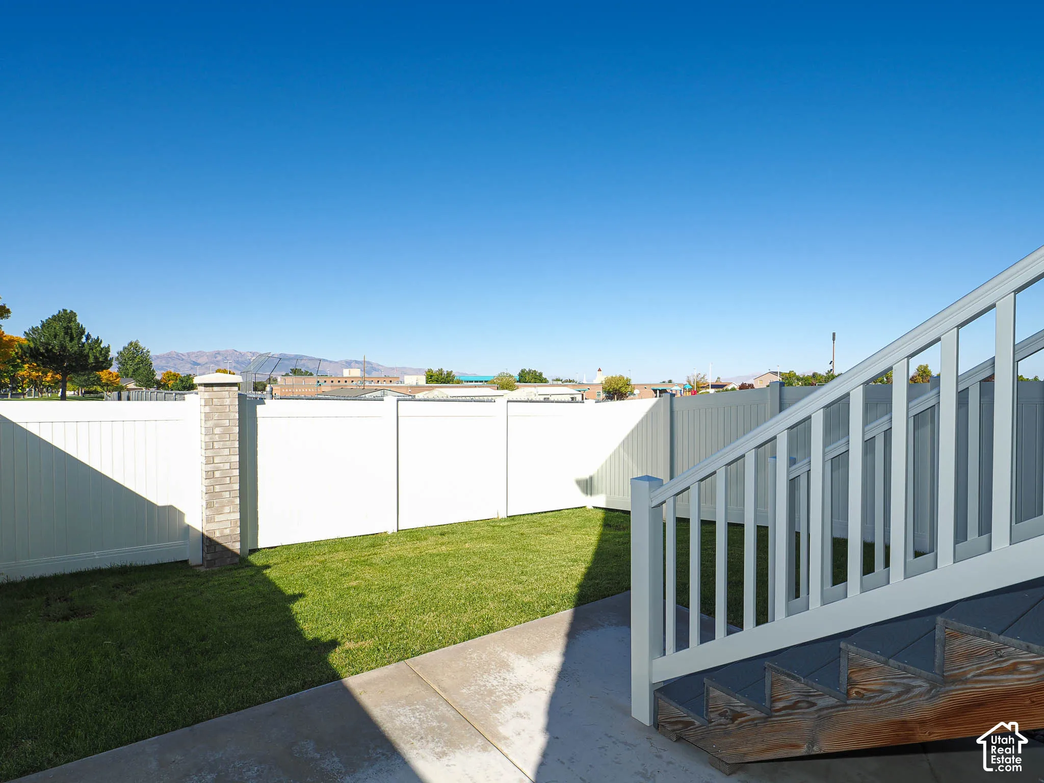 Fenced backyard featuring a manicured lawn, concrete patio, white vinyl privacy fencing, and exterior staircase with white railings