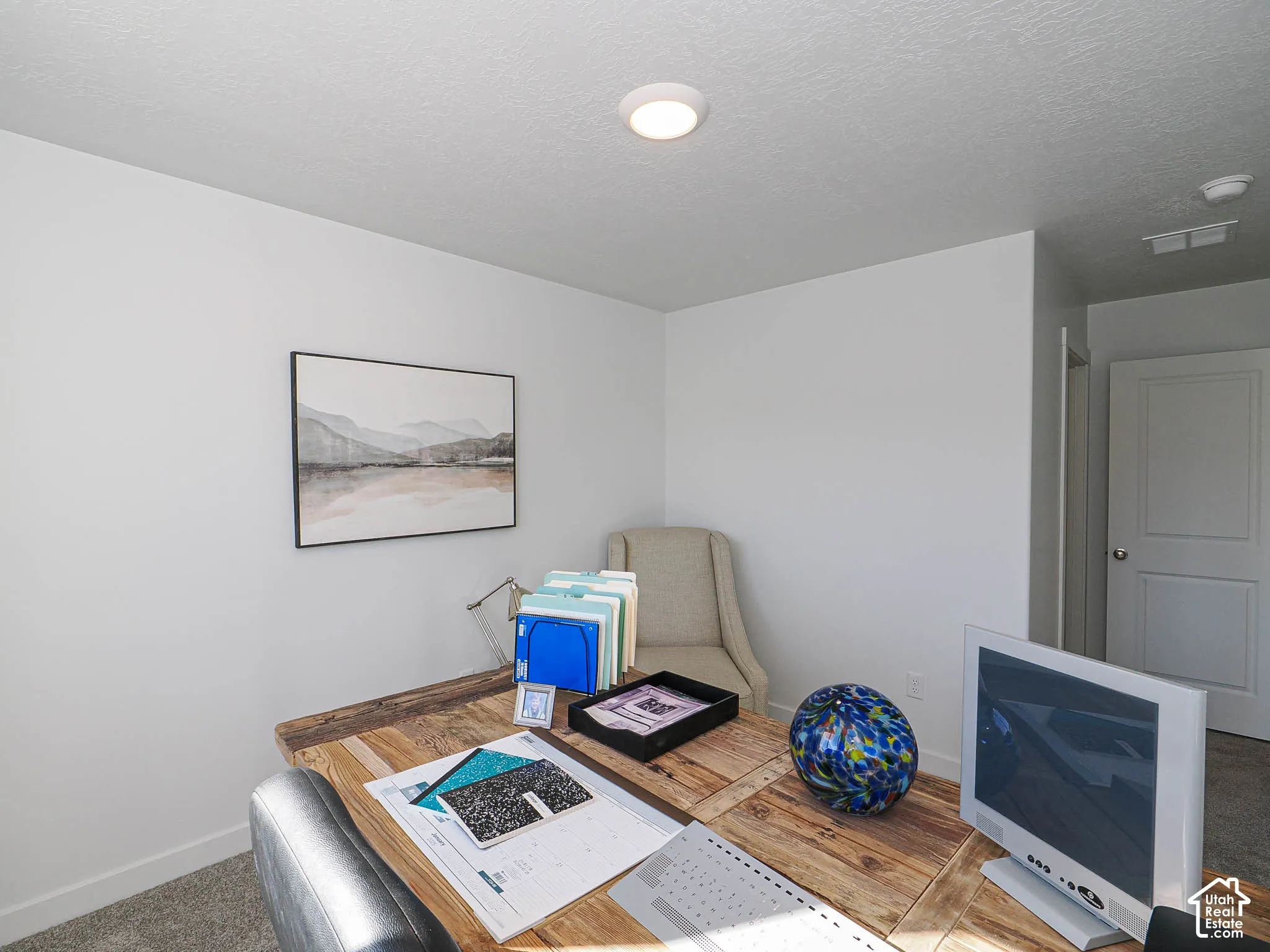 Neutral-toned interior space featuring neutral wall-to-wall carpeting, crisp white walls, a flush-mount circular ceiling light fixture, and a solid-core interior door with a silver-finish lever handle
