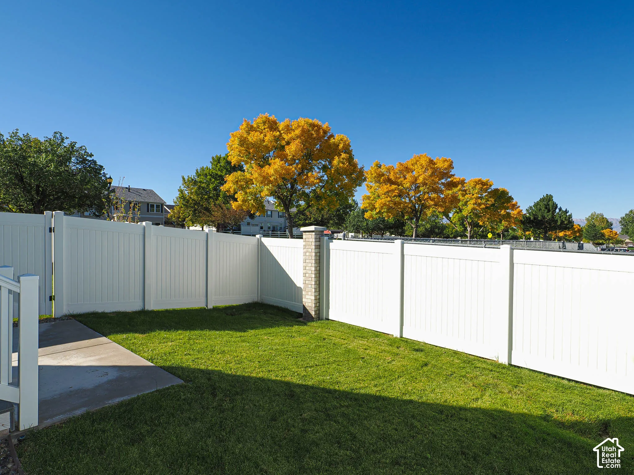 Backyard featuring a concrete patio, perimeter vinyl fencing, and a brick masonry post