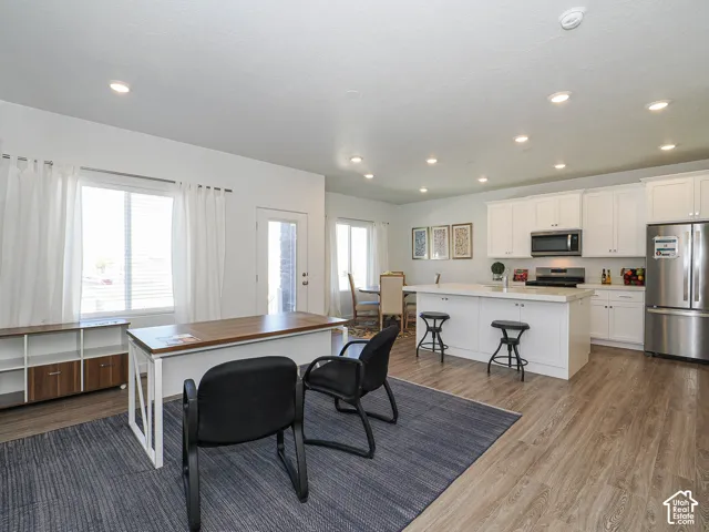 Open concept space featuring wood-finish flooring, recessed lighting, white shaker-style cabinetry, and a central kitchen island