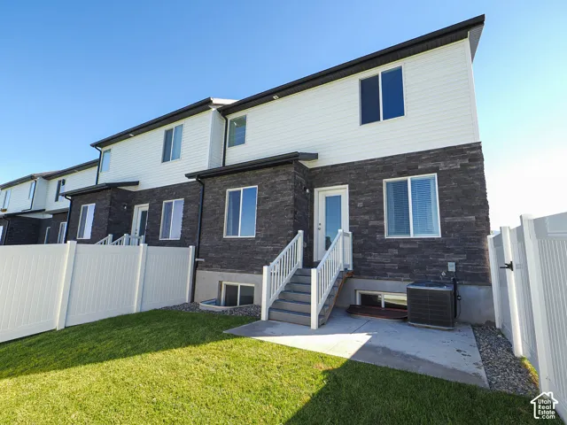 Exterior featuring horizontal siding, dark stone veneer, a concrete patio, white vinyl fencing, and staircase with white railings
