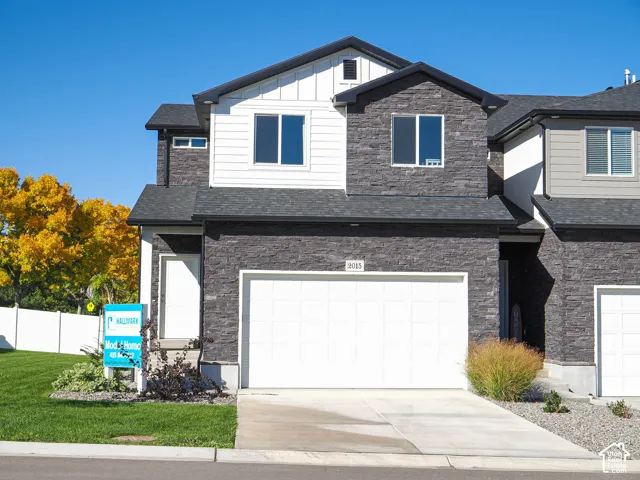 Two-story exterior featuring dark stone veneer siding, white vertical board-and-batten accents, a dual-pitched roofline, and an attached two-car garage