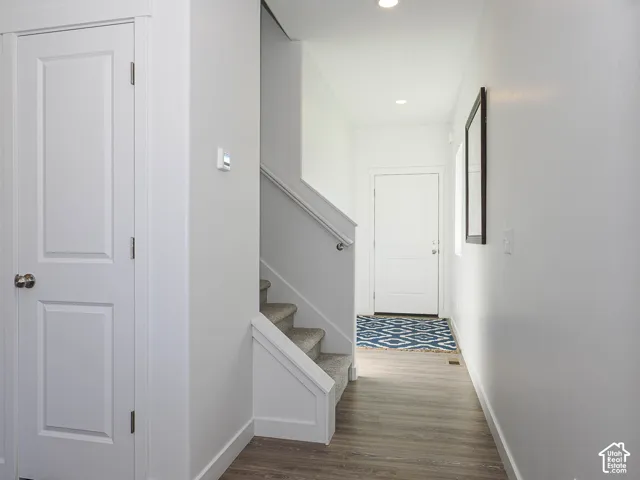 Entryway featuring wood-finish flooring, a paneled interior door, recessed lighting, and a staircase with a white handrail and carpeted treads