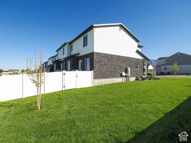 Multi-level exterior featuring white vinyl siding, dark stone veneer, a white vinyl privacy fence, and a manicured lawn