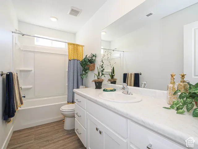 White vanity cabinet with an integrated sink, stone-finish countertop, full-width mirror, wood-finish flooring, and a combined tub and shower surround