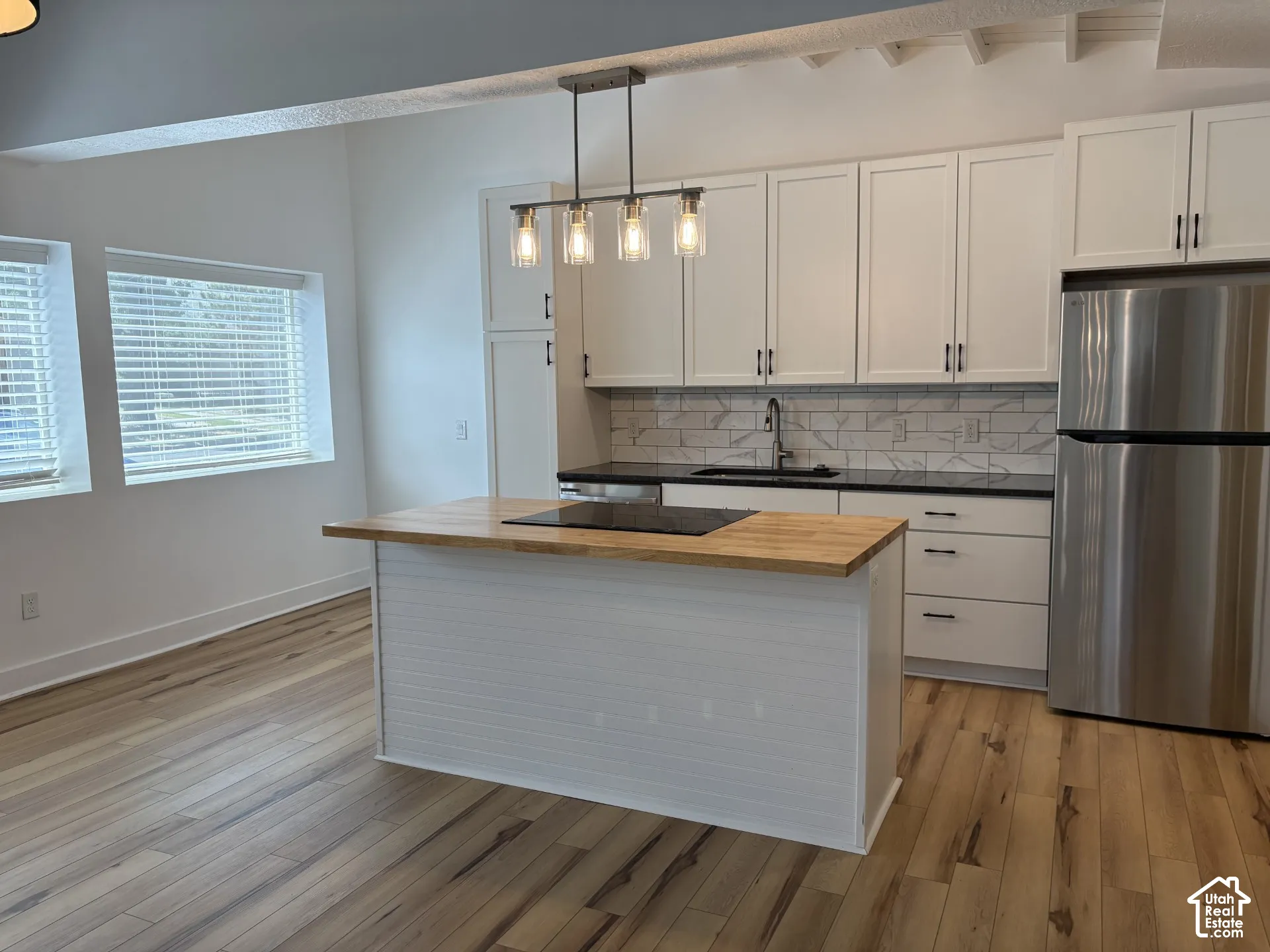 Kitchen featuring white cabinetry, wood-finish flooring, a butcher-block island countertop, dark solid-surface perimeter countertops, and a tile backsplash