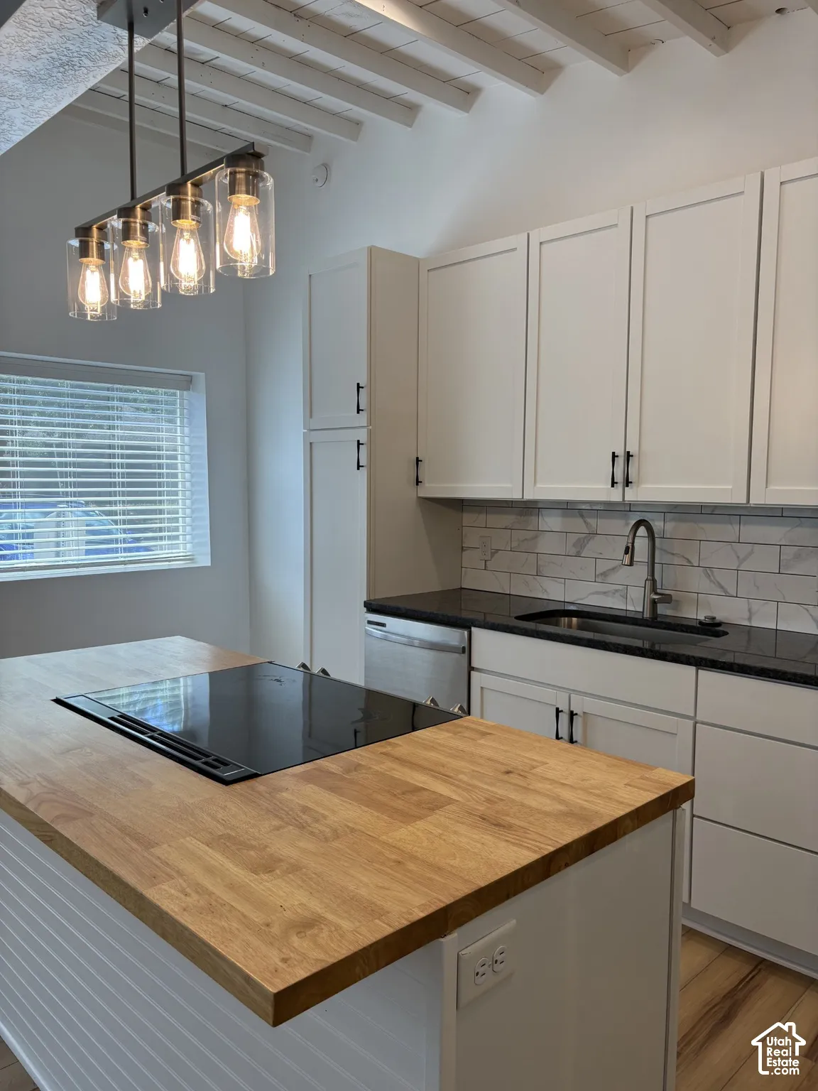 Kitchen featuring a central island with a wood-finish countertop and integrated cooktop, white shaker-style cabinetry, subway tile backsplash, and exposed ceiling rafters