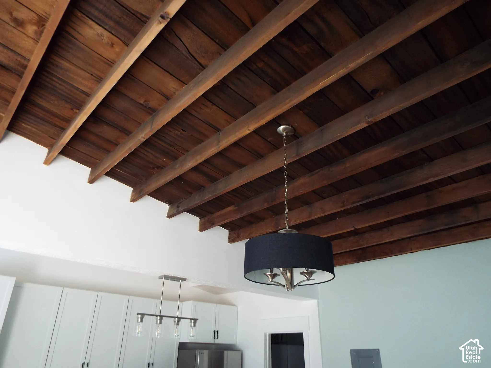Exposed wood ceiling beams, wood-plank ceiling finish, drum pendant light fixture, and linear multi-light fixture with glass shades