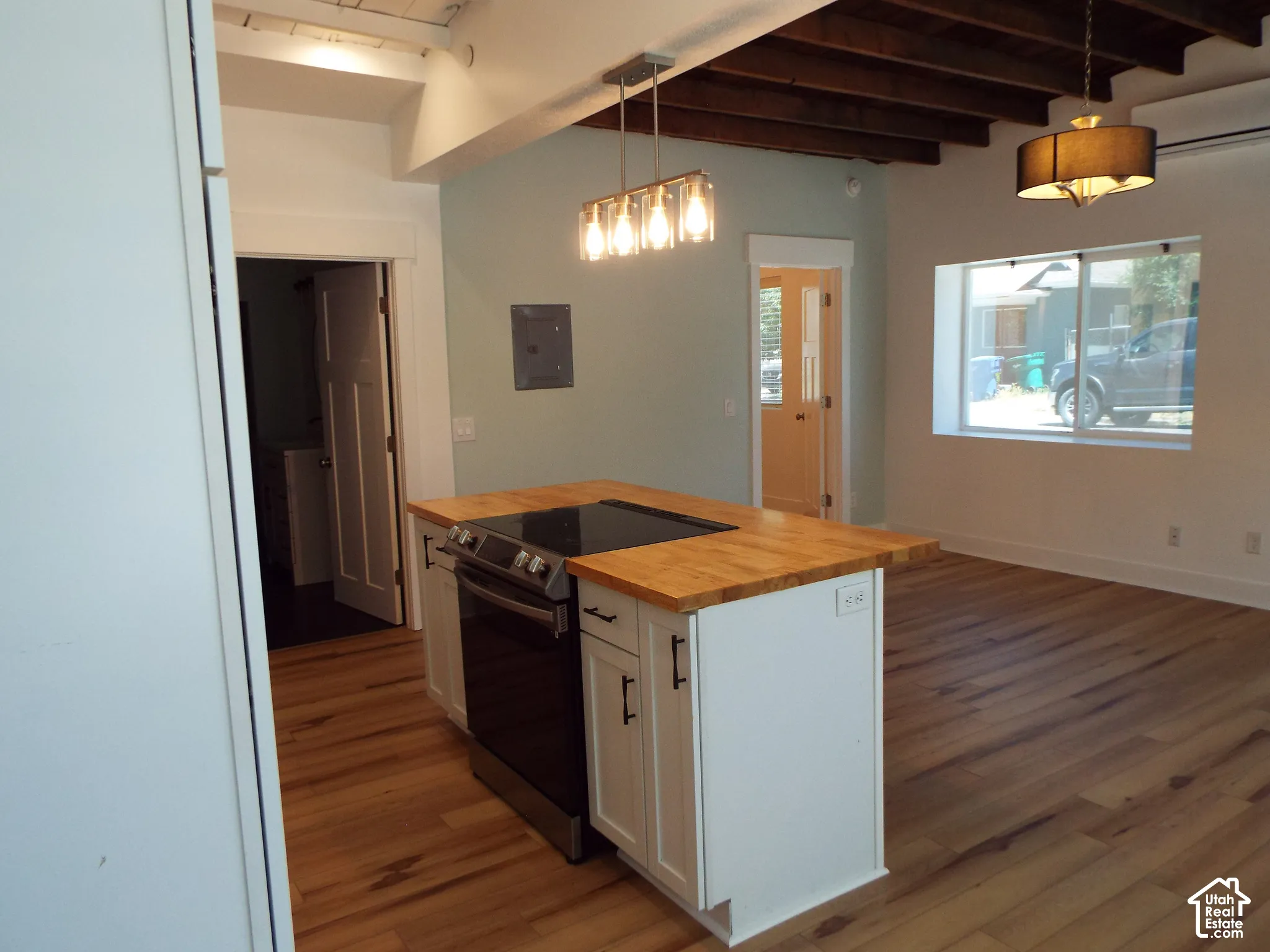 Kitchen island featuring a butcher-block countertop, integrated cooktop, white shaker-style cabinetry, and exposed dark wood ceiling beams