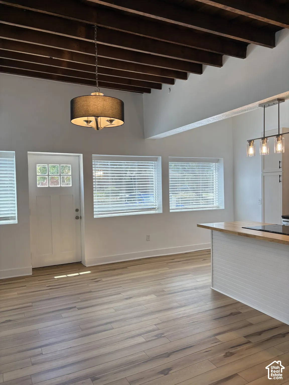 Exposed wood ceiling beams, wood-finish flooring, white beadboard kitchen island with a butcher block countertop, and dual pendant lighting fixtures