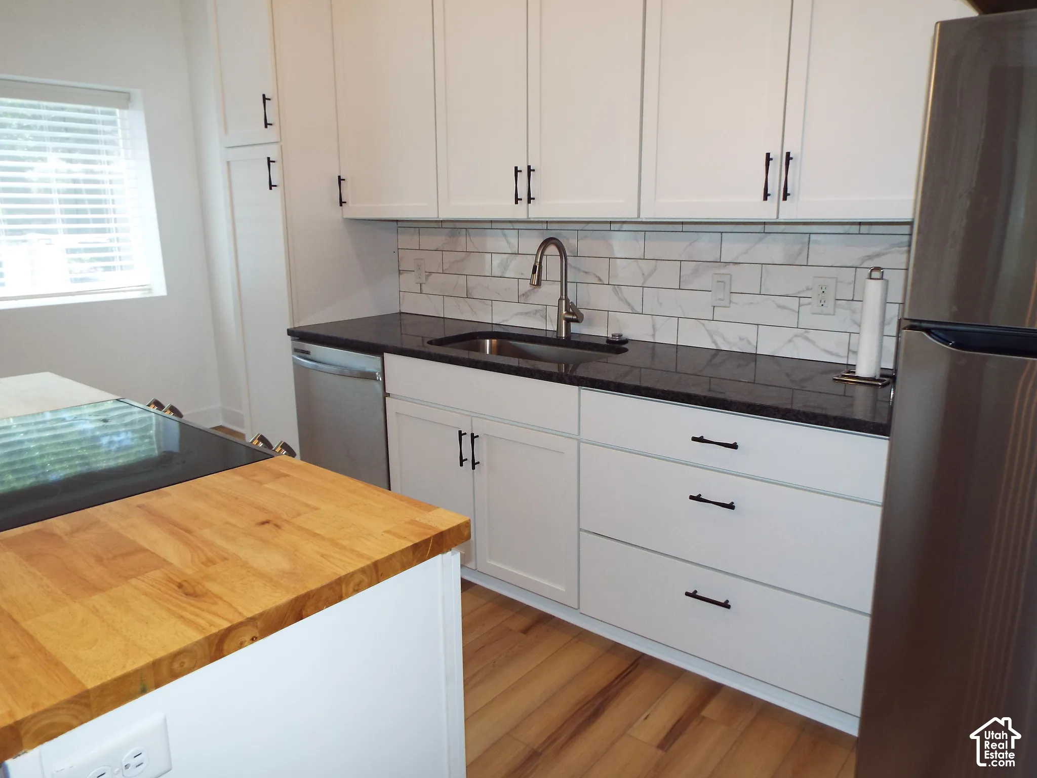 Kitchen featuring white shaker-style cabinetry, dark stone countertops, wood-finish island countertop, subway tile backsplash, and wood-finish flooring