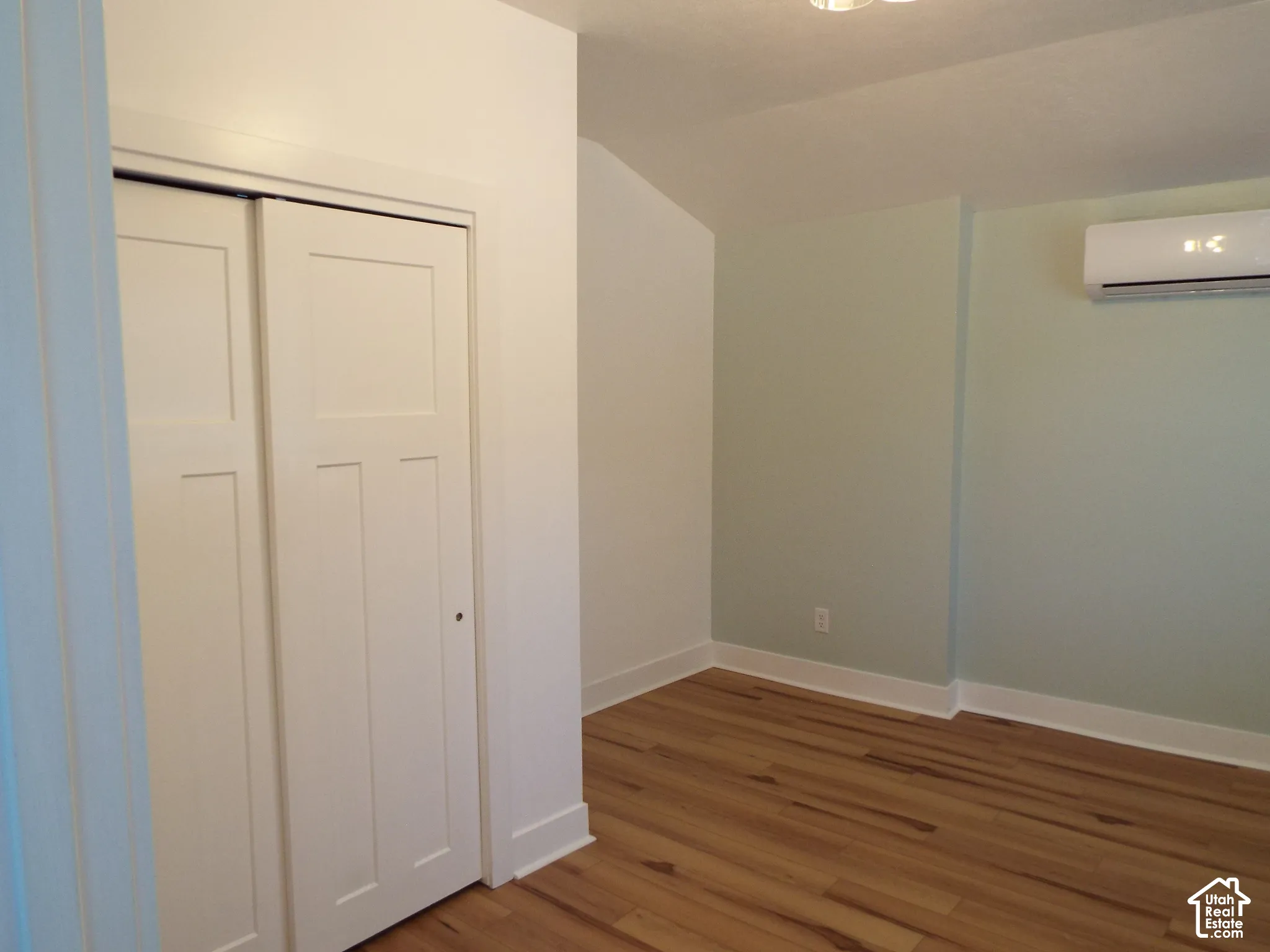Room interior featuring wood-finish flooring, two-panel bifold closet doors, and a wall-mounted ductless heating and cooling unit