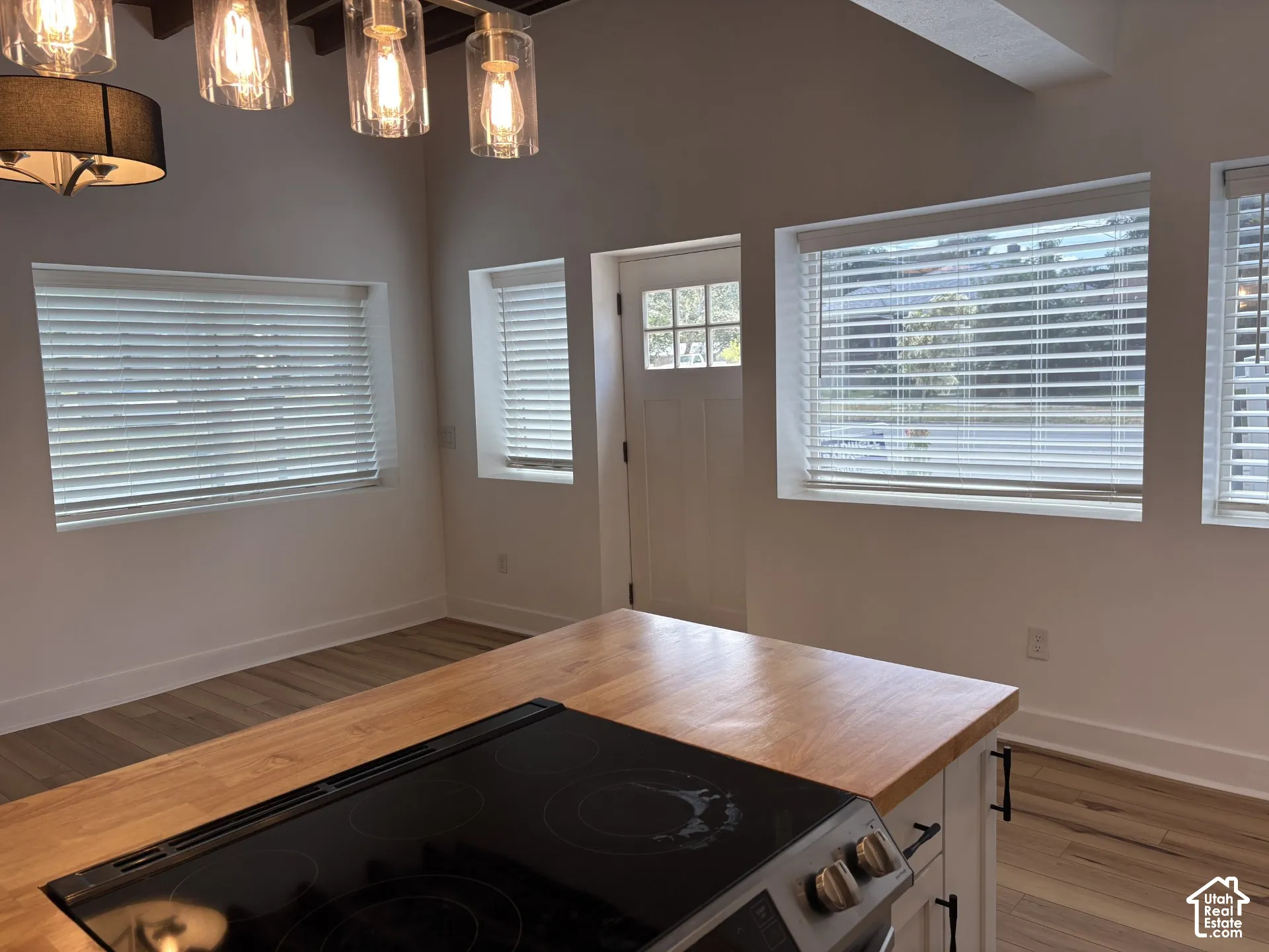 Kitchen island featuring a butcher block countertop, integrated electric cooktop, white cabinetry with matte black hardware, wood-finish flooring, and multi-light pendant fixture