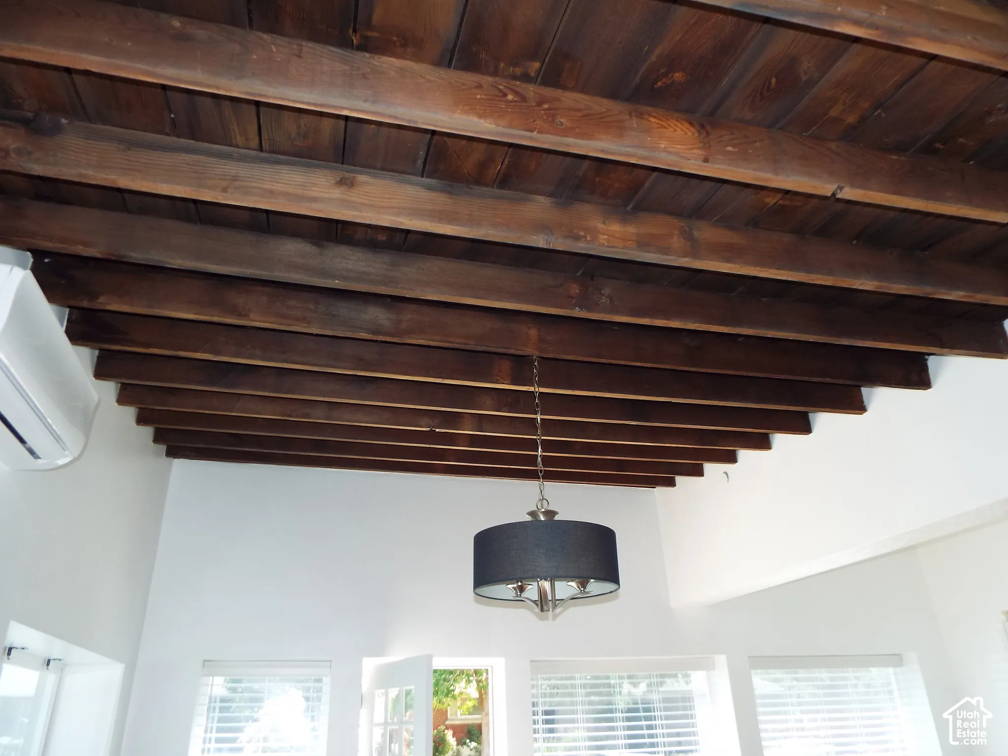 Exposed wood-beam ceiling featuring dark-finish timbers and a suspended drum-style light fixture