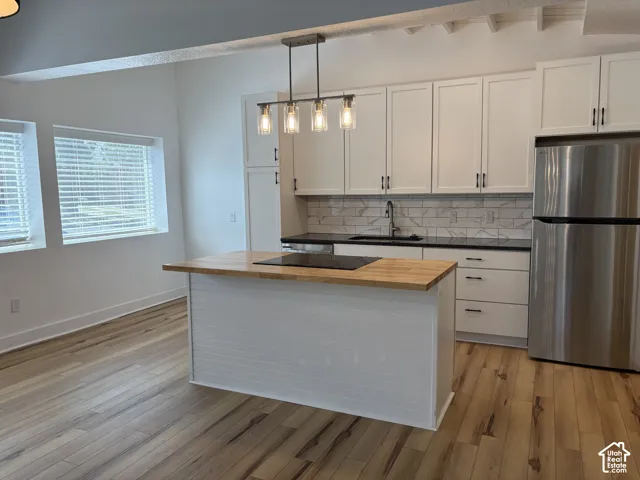 Kitchen featuring white cabinetry, wood-finish flooring, a butcher-block island countertop, dark solid-surface perimeter countertops, and a tile backsplash