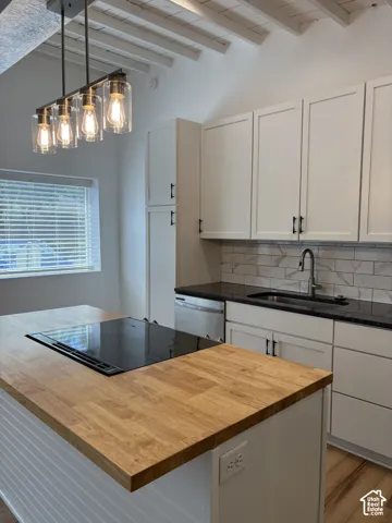 Kitchen featuring a central island with a wood-finish countertop and integrated cooktop, white shaker-style cabinetry, subway tile backsplash, and exposed ceiling rafters