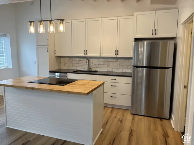 Kitchen featuring white cabinetry, dark countertops, a wood-finish island with a built-in cooktop, patterned subway tile backsplash, and stainless steel refrigerator