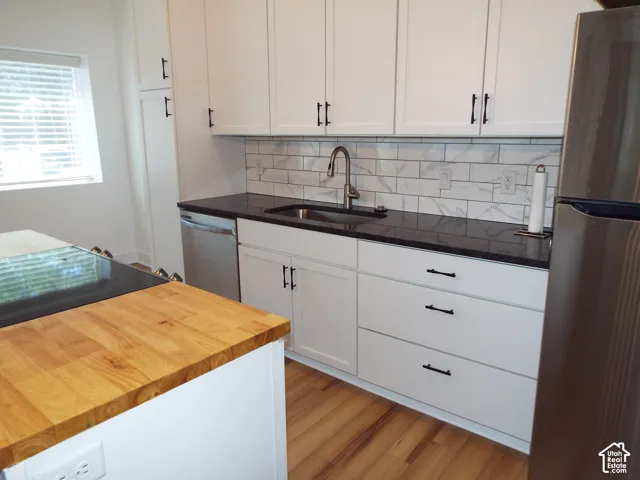 Kitchen featuring white shaker-style cabinetry, dark stone countertops, wood-finish island countertop, subway tile backsplash, and wood-finish flooring