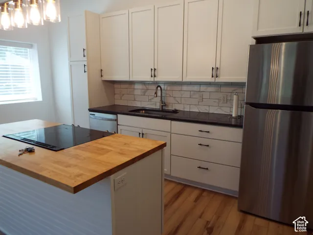 Kitchen featuring white shaker-style cabinetry, a wood-finish island countertop, dark stone-surfaced main countertops, a subway tile backsplash, and stainless steel appliances
