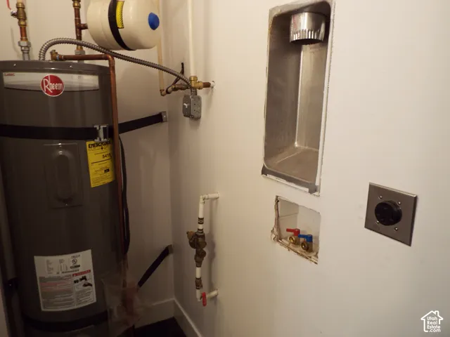 Utility area featuring a Rheem tank water heater, dedicated 220-volt electrical outlet, metal recessed dryer vent, and plumbing hookups for laundry appliances