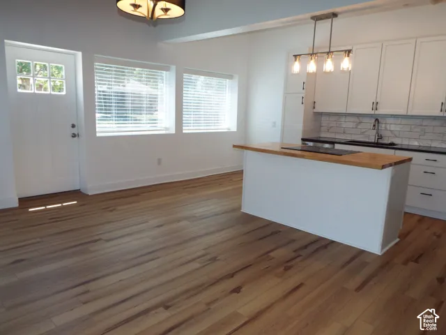 Wood-finish flooring, white shaker-style cabinetry, wood-top island, subway tile backsplash, and decorative pendant lighting