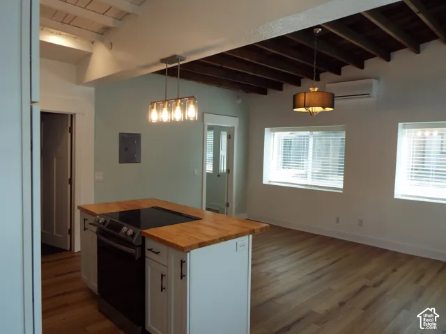 Kitchen featuring a butcher block countertop island with an integrated cooktop, wood-finish flooring, exposed ceiling beams, and pendant lighting