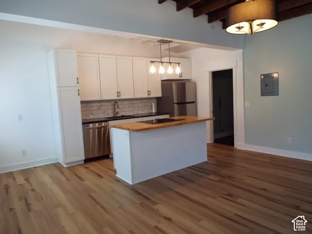 Kitchen featuring shaker-style cabinetry, wood-finish flooring, a butcher-block island countertop, subway tile backsplash, and exposed ceiling beams